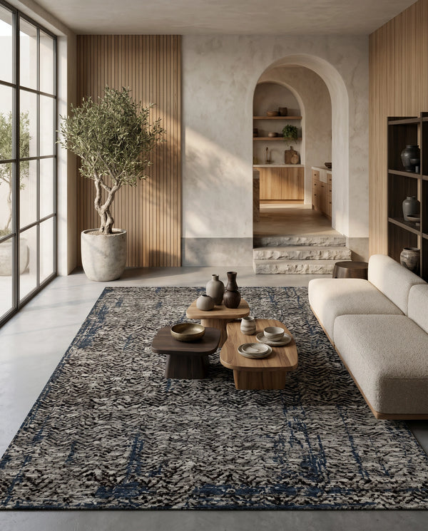 Charcoal and ivory chevron rug on a concrete floor with a cream sofa, wood coffee tables and a potted olive tree.