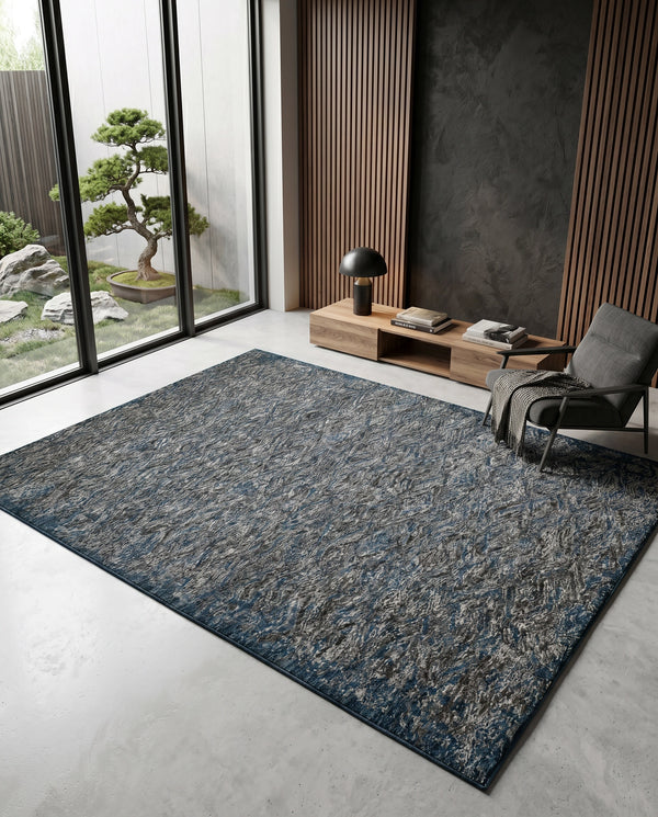 Blue and grey flecked rug on a concrete floor beside a grey armchair, low wood console and slatted timber wall.