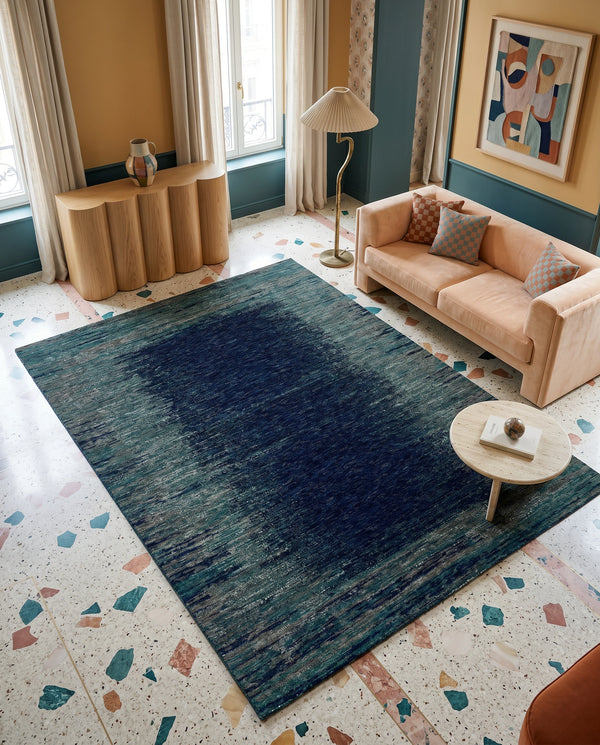Teal and navy rug on a terrazzo floor with a peach sofa, fluted wood console and pleated floor lamp.