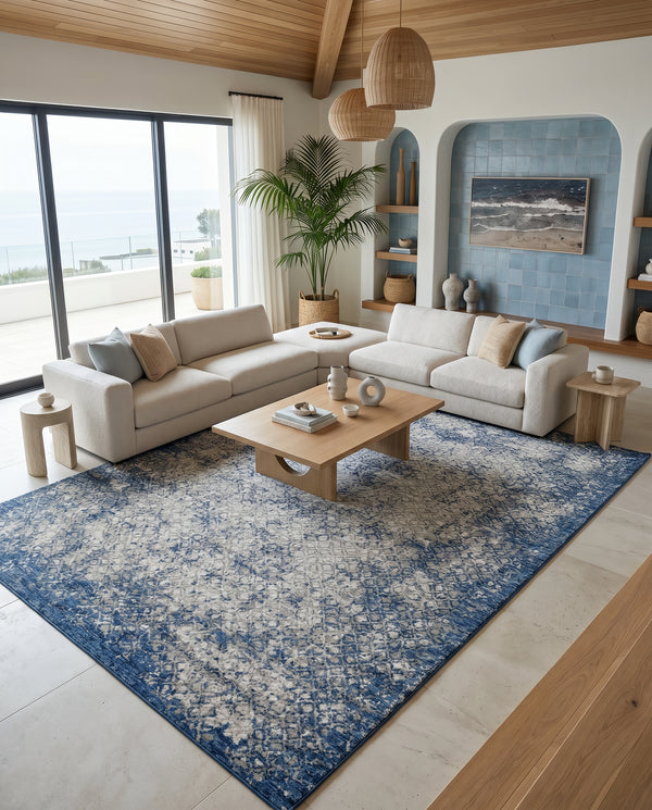Navy blue and grey rug in a coastal living room with a cream sectional, wooden coffee table and ocean view windows.