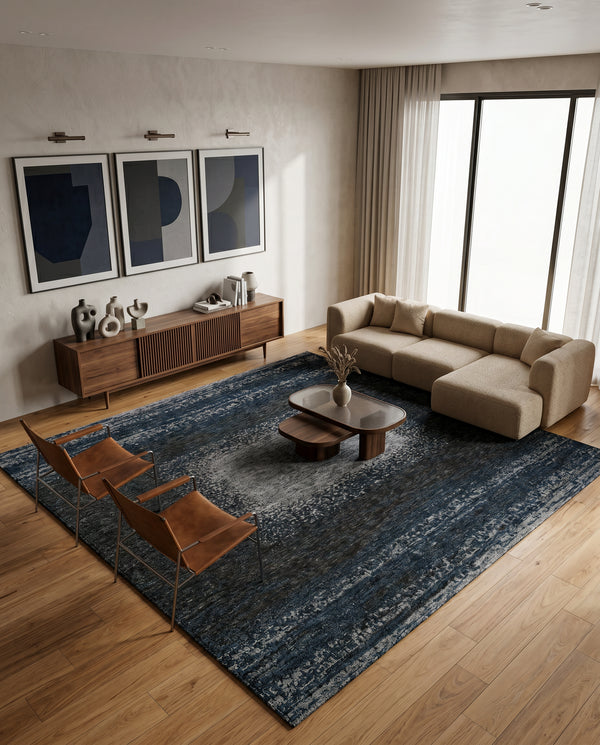 Dark blue rug on a wood floor with a beige sectional, two tan leather chairs, walnut sideboard and framed abstract prints.