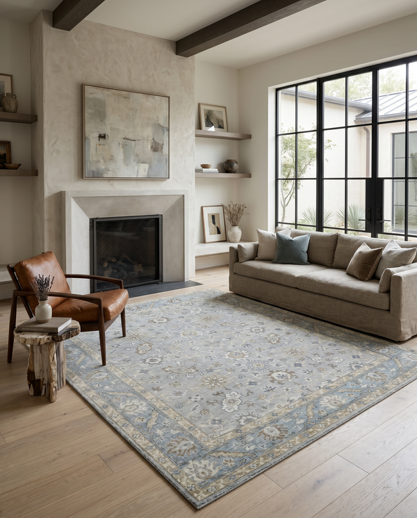 Light blue and beige floral rug on pale oak flooring with a linen sofa, leather armchair and plaster fireplace.